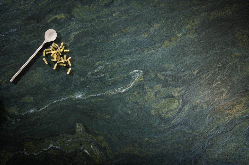Der olivgrün-gelbe Naturstein wird von dunkelgrauen Schattierungen durchsetzt, schimmert tiefgründig wie ein Gebirgsbach und erfrischt jeden Küchen-Korpus mit Eleganz und natürlichem Charme. Foto: STRASSER Steine