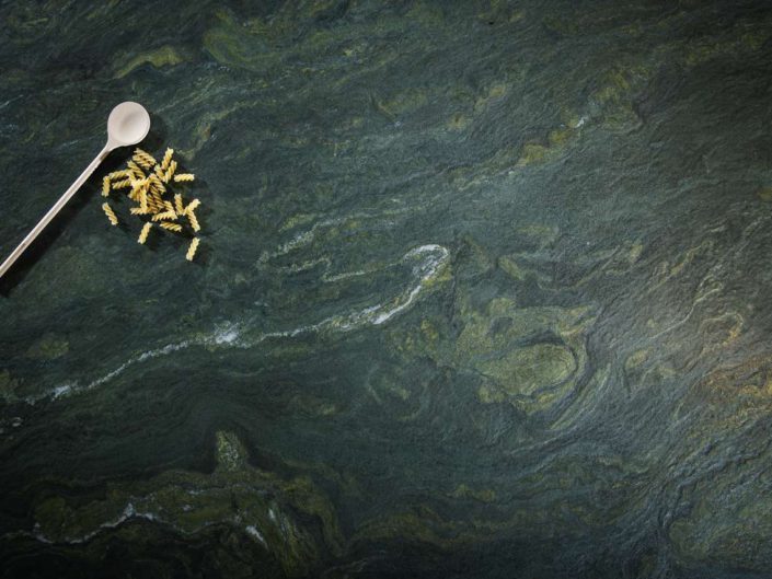 Der olivgrün-gelbe Naturstein "Alpengrün" wird von dunkelgrauen Schattierungen durchsetzt, schimmert tiefgründig wie ein Gebirgsbach und erfrischt jeden Küchen-Korpus mit Eleganz und natürlichem Charme. Foto: STRASSER Steine