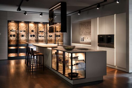 Die neue grifflose SieMatic wird im 2. Quartal 2019 bestell-und lieferbar sein. Im Mittelpunkt dieser Planung steht die großvolumige Insel mit filigraner Ceramic-Arbeitsplatte. Die Strenge der Formensprache und der Materialität wird durch zwei Elemente durchbrochen – durch die Transparenz der beleuchteten Unterschrankvitrinen mit schwarzmatt gebürsteten Metallrahmen und durch die elliptische Rundung der aufgesetzten Bartheke aus hellem Holz. Foto: ©SieMatic