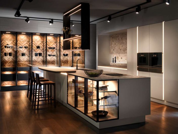 Die neue grifflose SieMatic wird im 2. Quartal 2019 bestell-und lieferbar sein. Im Mittelpunkt dieser Planung steht die großvolumige Insel mit filigraner Ceramic-Arbeitsplatte. Die Strenge der Formensprache und der Materialität wird durch zwei Elemente durchbrochen – durch die Transparenz der beleuchteten Unterschrankvitrinen mit schwarzmatt gebürsteten Metallrahmen und durch die elliptische Rundung der aufgesetzten Bartheke aus hellem Holz. Foto: ©SieMatic