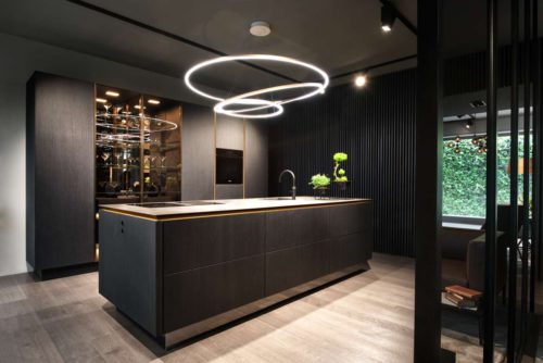 Typisch für die neue grifflose SieMatic ist das Spiel mit wechselnden Ebenen und mehreren Dimensionen. Besonders luxuriös erscheint die gekonnte Kombination aus schwarzmattem Echtholz-Furnier, goldbronze eloxiertem Aluminium, dezent getöntem Glas und verspiegelten Oberflächen. Die in parsolbronze getönten Glastüren der Hochschrankvitrinen geben bei eingeschalteter Beleuchtung den Blick auf die edle Materialität des Innenraums frei. Foto: ©SieMatic