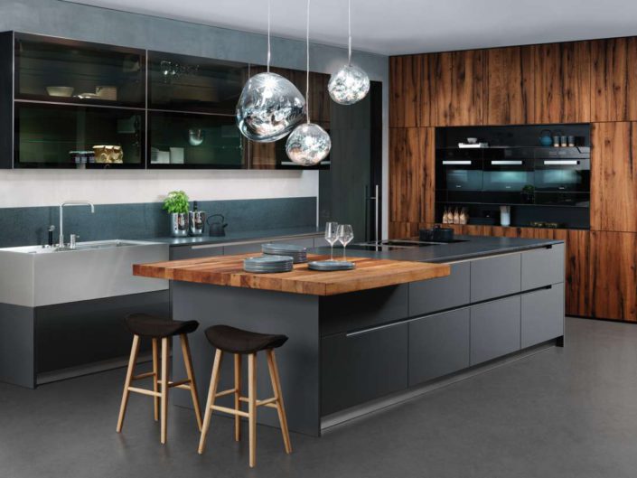 Wer sich für die Kombination aus „anthracite" und „old oak" entscheidet, setzt auf den rauen Charme klassischer Moderne. Graue Unterschrankfronten, Edelstahlelemente und bronzefarbiges Dekorglas wirken verführerisch einladend. Dunkle, sockelüberdeckende Furnierfronten und die Arbeitsplatte aus Naturstein setzen stimmige Kontraste. Foto: INTUO