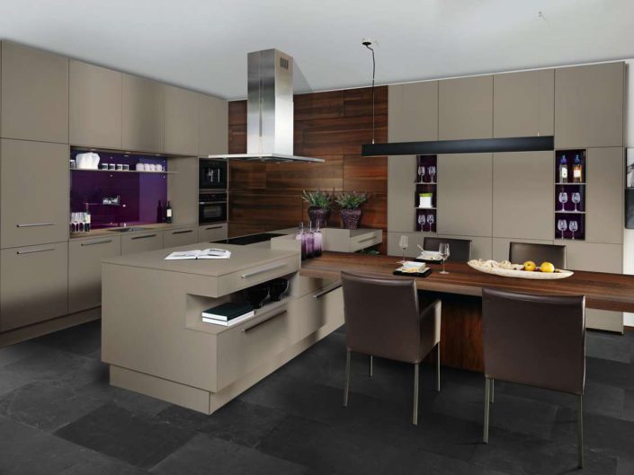 Harmonischer und eleganter Farb- und Materialmix mit dem Dekor fango und den edel furnierten Holzfronten in nuss. Zusätzliche attraktive Features – wie das Regalsystem „Conception 12“, die 6 cm starke Thekenplatte in Echtholzfurnier als Esstisch oder die sockelüberdeckenden Fronten hinter dem Essbereich – runden den Gesamteindruck dieses Modells ab. Foto: ewe