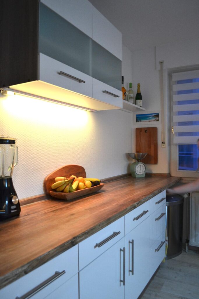 Wenn der Abend angebrochen ist erstrahlt die Küche dank der versteckten LED-Leisten unterhalb der Oberschränke in einem ganz neuen Licht. Ob lila, orange oder einfach nur weißes Arbeitslicht - dank der Farbwechselfunktion herrscht hier immer das richtige Licht für die richtige Stimmung. Übrigens hat sich das Ehepaar für eine Ablufthaube entschieden, der dafür benötigte Abluft-Mauerkasten war glücklicherweise bereits vorhanden. Foto: Küchen Journal