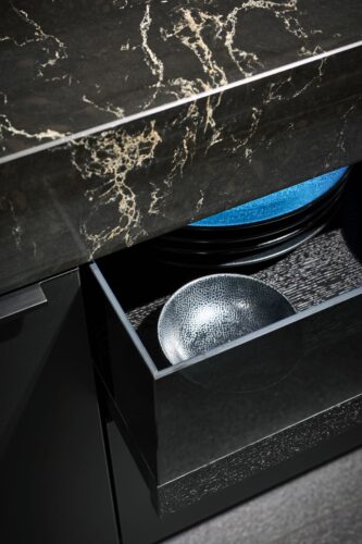 Dieses Premium-Wohnküchen-Design setzt anstelle von Glasschränken auf extravagante Vitrinenauszüge als „Schaukasten“ – ein tablettartiger Auszug aus Holz, der mit einem dunklen Glaskubus veredelt ist. Foto: AMK