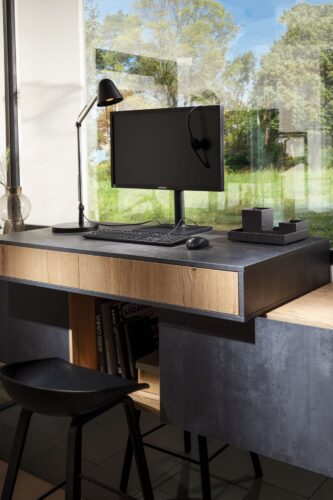 Die Küchenfronten aus graphitfarbenem Spachtelbeton setzen den Schreibtisch in Szene. Durch Schublade, Regal und Schrank hat er genügend Stauraum. Foto: Häcker