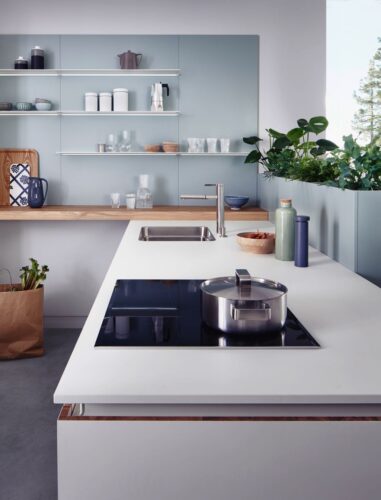Landhaus meets Skandi-Style: Die schlichte Küche wirkt durch die Holzplatte und die Metallregale richtig wohnlich. Auch die Grünpflanzen prägen den Stil. Küche von Leicht. Foto: Leicht