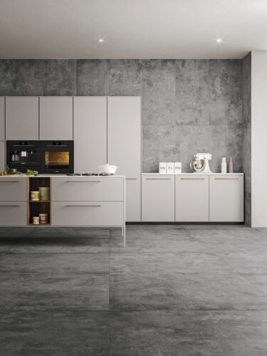 Minimalistisch ist diese Wand in der Küche gehalten. Die große, moderne Fliese „Urbex Style“ in Grey ist nicht nur auf dem Boden verlegt, sondern bis unter die Decke verwendet worden. Nur hat sie andere Maße als die Fliese am Boden. Von Ceramiche Refin.