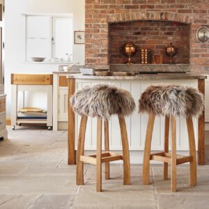 Sieht schön aus und wärmt noch: Legen Sie hübsche Felle oder Fellkissen auf die Stühle. Alternativ wärmen auch Samt- oder Strickkissen.
Die Hocker fallen mit ihren tollen Fellkissen gleich ins Auge. „Gwyn Baa Sheepskin Bar Stool“ von Lime Lace.