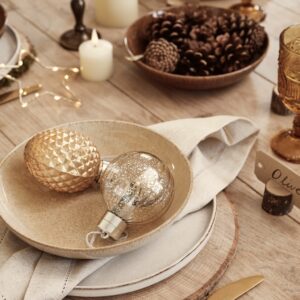 Ein Hingucker sind die Holzscheiben, die als Set dienen. Passend ist die tolle DIY-Idee, die Tischkärtchen aus einem Holzstämmchen selbst zu gestalten. Das i-Tüpfelchen sind aber das goldfarbene Besteck und die glanzvollen Kugeln.