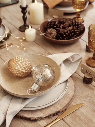 Ein Hingucker sind die Holzscheiben, die als Set dienen. Passend ist die tolle DIY-Idee, die Tischkärtchen aus einem Holzstämmchen selbst zu gestalten. Das i-Tüpfelchen sind aber das goldfarbene Besteck und die glanzvollen Kugeln.
