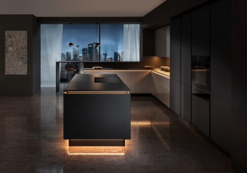 Hier wirkt die Beleuchtung sehr harmonisch. Sowohl die Insel, als auch die restliche Arbeitsfläche sind stilvoll durch das indirekte Licht in Szene gesetzt. Einen modernen Akzent setzen die beiden Design-Leuchten im Essbereich. Die elegante Fronten-Kombi gehört zur Serie „Iseo" von Rempp Küchen.