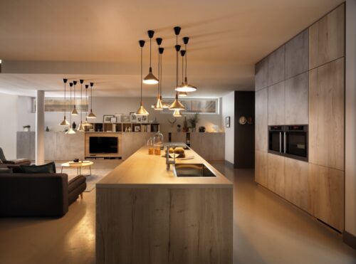 Wunderschön harmoniert der eher kühle Betonlook mit dem robusten, atmosphärischen Holz und der warmen Beleuchtung. Ganz konsequent wird der Stil für den gesamten Raum genommen. Aus der Kollektion „Arcos“ von Schmidt Küchen.