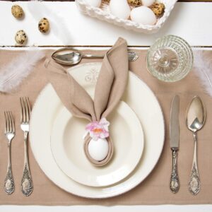 Niedliche Idee für die Festtafel: Falten Sie eine schlichte Leinenserviette so, dass sie sich als Hasenohren um ein Ei legen lässt. Noch eine Blüte daran stecken und schon strahlt Meister Lampe vom Teller. Alles von IHR.