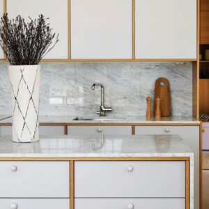 Sehr minimalistisch sieht die Küche aus, die hauptsächlich vom Scandi-Stil bestimmt ist. Doch wer genauer hinsieht, bemerkt die etwas üppigeren Details wie die Marmor-Elemente, die Knauf-Griffe und die aufwändige Holzeinfassung.