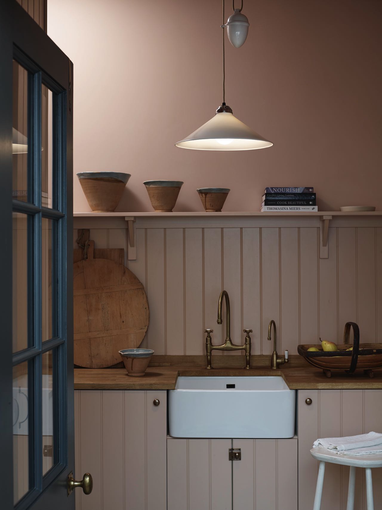 Die Küche im Shaker-Stil bildet eine komplette Einheit mit der Wand. Die Farbe liegt irgendwo zwischen Rosa und hellem Braun. Super schön dazu: die matten Armaturen, Holz- und Keramik-Accessoires. Die stylishe Lampe „Cobb“ ist von Original BTC.