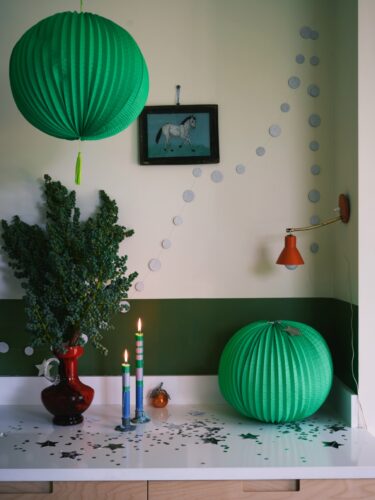 Die Papierkugeln samt Konfetti und Punktgirlande haben einen echten Partycharakter. Durch die Farbigkeit passen sie zu Weihnachten, ohne schwer und traditionell zu wirken. Die Wandfarbe ist von Farrow & Ball.