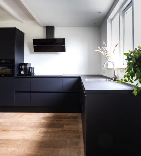 Schön puristisch ist diese grifflose Küche mit matten Fronten in Schwarz. Die rustikalen Holzdielen bringen optische Wärme in den Raum. Foto: Sven Brandsma | Unsplash