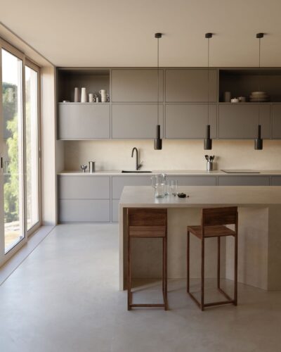 Der Boden in Betonoptik  harmoniert perfekt mit der minimalistischen, hellgrauen Küchenfront. Die Kücheninsel aus Dekton® von Cosentino mit ihrer marmorierten Optik setzt einen attraktiven Kontrast.