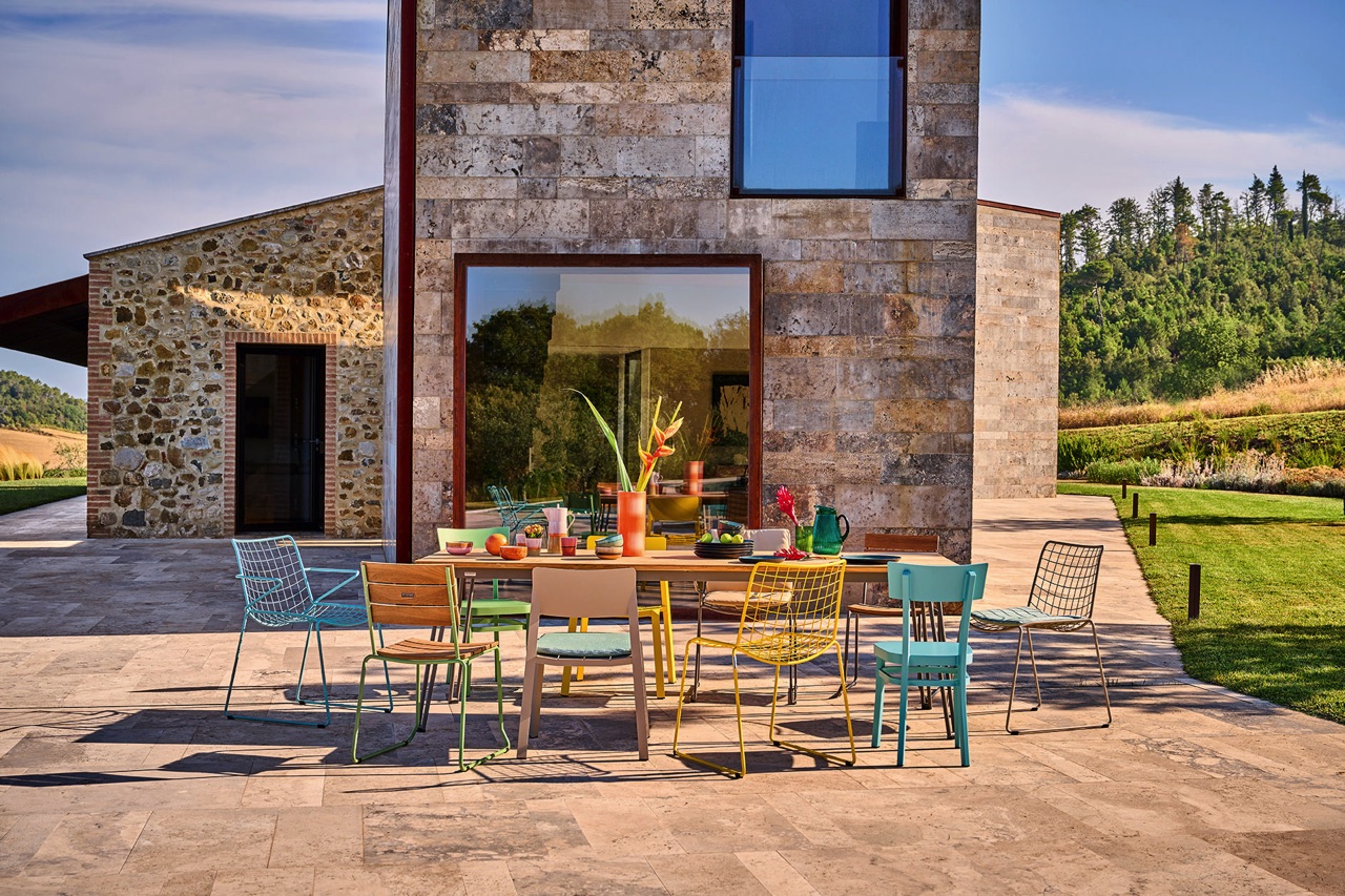 Ein bunter Mix an Stühlen ist eine sehr individuelle Idee und bringt Fröhlichkeit auf die Terrasse. Die Gitter- und Holzstühle werden mit Kissen richtig gemütlich. Der große Tisch wirkt einladend. Alles von Weishäupl.