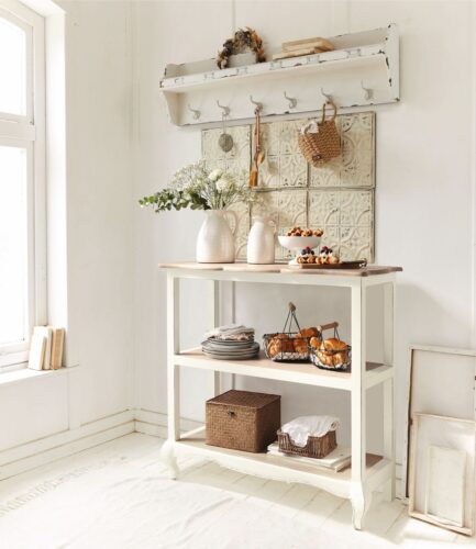 Landhaus, aber bitte gemütlich! Das erreicht man mit Details. Die Anrichte dient als Ablage und Fläche für Deko-Elemente, wie eine Vase. Die Haken schaffen zusätzlichen Stauraum, das Shabby-Regal sorgt für eine persönliche Note. Alles von Loberon.
