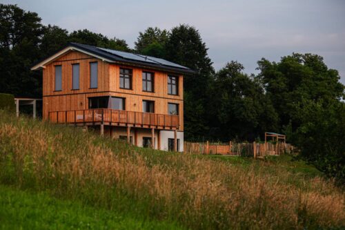 Lenas und Stefans Holzhaus erstrahlt in voller Pracht, harmonisch eingebettet in die sanften grünen Hügel der Steiermark