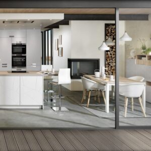 Wie gemütlich der Raum gestaltet ist mit dem Kamin und dem großzügigen Lagerplatz für das Holz. Ein Blickfang sind die geometrisch designten Fronten in schlichtem Weiß. Die Küche ist aus der Linie „Arcos Lazer“ von Schmidt.