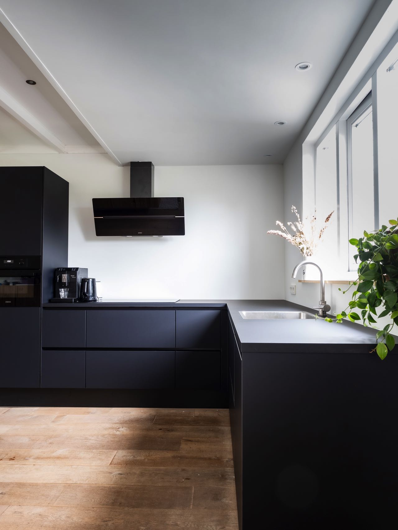 Die vollkommen in Mattschwarz gehaltene grifflose Küche, ergänzt durch eine kopffreie Dunstabzugshaube und akzentuiert durch passende schwarze Küchengeräte, verkörpert minimalistische Eleganz in seiner reinsten Form.