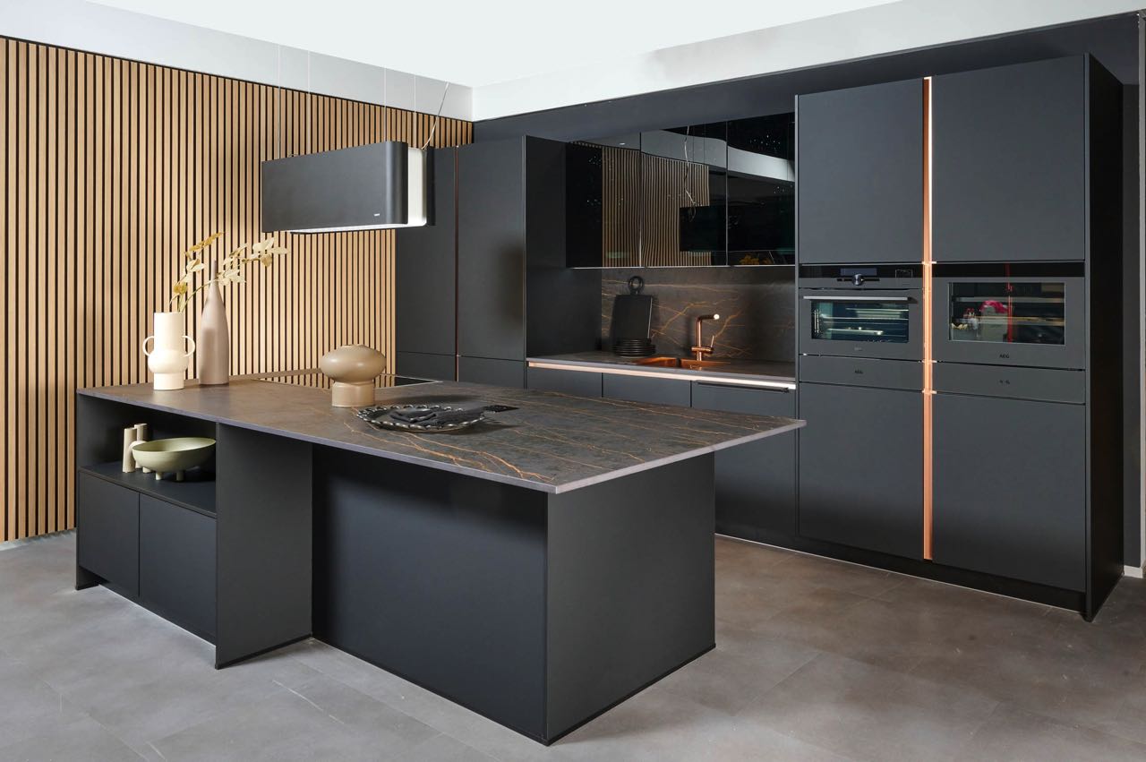 Die vertikal angebrachten Holzpaneelen bringen Wärme in diese moderne Küche von Impuls Küchen. Die Wand harmoniert perfekt mit den Kupferdetails und bieten einen angenehmen Kontrast zum kühlen Schwarz und Grau der Einrichtung. 