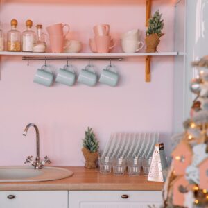 Das zarte Pastellrosa der Wandgestaltung setzt in dieser heimeligen Landhausküche ein sanftes Highlight. Es schafft eine harmonische Verbindung zwischen den weißen Küchenmöbeln und den türkisen Akzenten, wie den Tassen und dem Retro-Kühlschrank. Die liebevoll platzierten Weihnachtsdekorationen unterstreichen die warme Atmosphäre und laden zum gemütlichen Verweilen in der festlichen Jahreszeit ein. Foto: Eugenivy by Unsplash