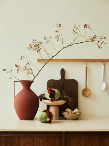 Ein einzelner Zweig ist ein Hingucker in der schlichten Terracotta-Vase. Ebenfalls herbstlich ist das blumige Kürbis-Arrangement. Dafür werden Trockenblumen in einen ausgehöhlten Kürbis gesteckt. Foto: Toll was Blumen machen