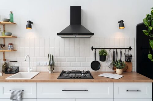 Die schlichte Eleganz dieser weißen Landhausküche wird durch stilvolle schwarze Akzente und angesagte Metro-Fliesen an der Wand akzentuiert. Die Kombination aus einer Arbeitsplatte in Holzoptik und dem klaren Weiß der Schränke schafft eine warme, einladende Atmosphäre, während die hängenden Utensilien Praktikabilität und rustikalen Charme verleihen. 