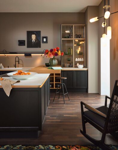 In dieser eleganten Landhausküche von Nolte Küchen verschmilzt traditioneller Charme mit modernem Wohnkomfort. Die Glasvitrine, ein klassisches Element des Landhausstils, präsentiert sich hier in einem schlanken, zeitgenössischen Design und bietet stilvollen Raum für feines Geschirr und Dekorationsobjekte.