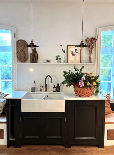 Der Keramikspülstein, ein Klassiker in Landhausküchen, bildet einen harmonischen Kontrast zu den maßgefertigten, schwarz lackierten Vollholzschränken.