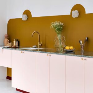 Wer sich gegen Regale oder Schränke an der Wand entscheidet, hat neu gewonnenen Platz für eine hübsche Gestaltung. In diesem Fall ist das eine kunstvoll bemalte, farbige Wand mit Lampen. Küche von Plum Living.