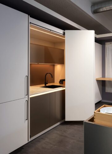 Eine riesige Schrankwand bietet Rempp, unter anderem mit dem 3-türigen Schrank mit sogenannten Pocket-Türen. Die Türen lassen sich schieben, beim Öffnen kommt dann die Küchenzeile mit Spüle zum Vorschein. 