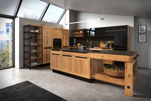 Diese Holzküche von Decker IPM Möbelwerke verbindet industrielles Flair mit natürlicher Wärme. Die hochwertige Arbeitsplatte und die Oberschränke mit schwarzen Glasfronten bieten einen modernen Kontrast zur Authentizität des echten Holzes. Das Design stellt eine gelungene Symbiose aus robustem Industriestil und der Gemütlichkeit von Naturmaterialien dar.