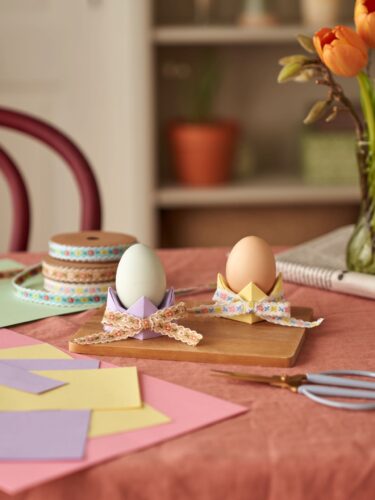 Es gibt viele niedliche Eierbecher, doch ganz besonders ist es, sie selbst herzustellen. Das gelingt mit buntem Tonpapier in den Maßen 15 x 15 Zentimetern, Schleifenband und der richtigen Origami-Technik. Verständliche Anleitungen findet man zum Beispiel bei YouTube. Das i-Tüpfelchen für die Eierbecher sind die bunten Bänder von Søstrene Grene. 