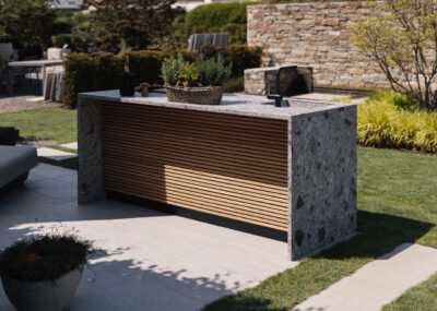 Von Cubic Outdoor Living gibt es kleine Lösungen für die Outdoor-Küche, die dennoch in Sachen Eleganz kein Kompromiss sind. Dieses Modell ist mit der angesagten Rillen-Anmutung in Szene gesetzt, so wirkt alles zeitgemäß. Hilfreich ist die großzügige Arbeitsfläche. Durch die Form der Insel kann man auch mit Barhockern direkt an der Platte essen, das ist sehr kommunikativ.