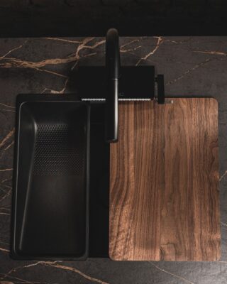 Wetterfest und sehr ästhetisch ist die Oberfläche Dekton „Laurent“ von Cosentino. Sie kann also auch bei der Outdoor-Küche zum Einsatz kommen. Der dunkle Untergrund und die goldfarbenen Adern wirken elegant. Da passen das schwarze Becken und das Schneidebrett aus Nussbaum-Holz ideal dazu.