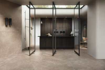 Nicht ganz typisch kommt der Industrie-Look zur Geltung, verschiedene Elemente machen ihn dennoch aus, zum Beispiel die flexiblen Glastüren. Ein Hingucker sind die großformatigen, eleganten Steinfliesen von Refin Ceramiche. In ihren Fugen kann sich kaum Schmutz absetzen.