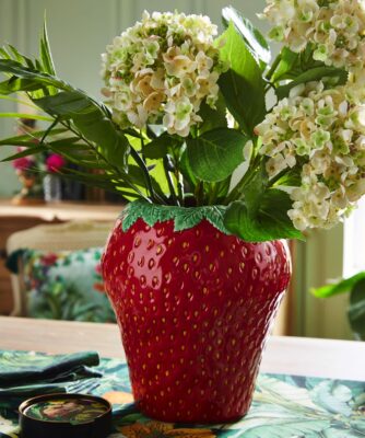 Blumen machen den gedeckten Tisch erst komplett. Aktuell sehr angesagt sind Vasen in Form von Früchten. So auch die rote Keramik-Erdbeervase, die einen schönen Kontrast zu den weißen Hortensien bildet, von Joe Browns.