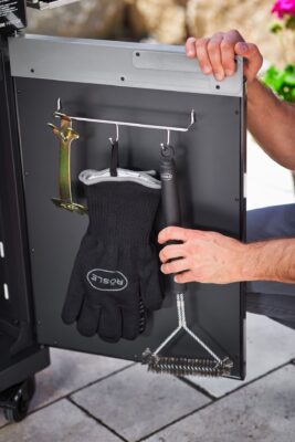 Sehr sinnvoll ist es, wenn man beim Grillen alles gleich griffbereit hat. Im Unterschrank des Grills lässt sich eine Seitenleiste installieren. Dort können Handschuhe und Grillzubehör aufgehangen werden, von Rösle. 