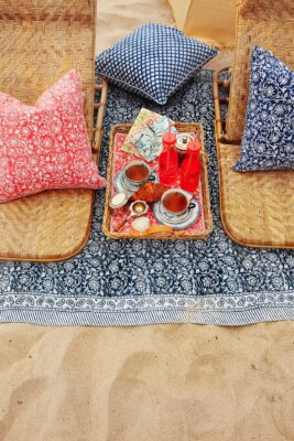 Ein Strand-Picknick mit ganz elegantem Charakter, das ist mit den Textilien im französischen Stil von Chamois garantiert. Die niedlichen Muster wirken verspielt und harmonieren in Blau und Koralle perfekt miteinander. Besonders praktisch sind auch die Rattanstühle, an die man sich bequem anlehnen kann.