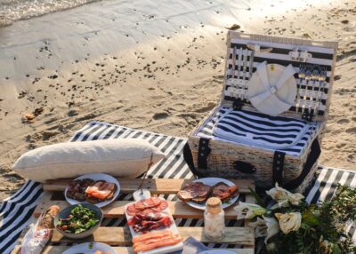 Der geräumige Picknickkorb kommt mit maritimem Flair daher und ist damit genau passend für das Picknick am Meer. Praktisch ist die integrierte Kühltasche. Die Decke im Streifenlook sieht attraktiv dazu aus. Der Inhalt eines solchen Korbs reicht für etwa vier Personen, von Les Jardins de la Comtesse.