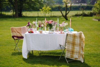 Wer eine romantische Sommertafel decken möchte, sollte vor allem die Blumen nicht vergessen. Rosen und Wiesenblumen in pastelligen Farben passen zu diesem Look. Niedlich sieht es aus, wenn Sie die Blüten in kleine Glasvasen in zarten Farben stellen. Dazu harmoniert Geschirr mit Blumenmotiven und eine weiße Tischdecke. Die hübschen gedrehten Kerzen sind von Talking Tables.