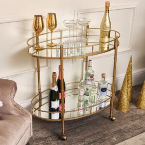 Der Barwagen mit goldenem Spiegel ist ein dekoratives Möbelstück und noch dazu praktisch für die Homebar. Er kann bequem hin und hergerollt werden. Seine Art-déco inspirierte Optik macht ihn besonders. Gefertigt aus Metall und Glas von Melody Maison.
