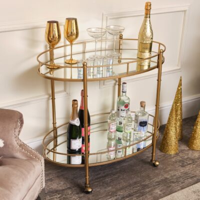Der Barwagen mit goldenem Spiegel ist ein dekoratives Möbelstück und noch dazu praktisch für die Homebar. Er kann bequem hin und hergerollt werden. Seine Art-déco inspirierte Optik macht ihn besonders. Gefertigt aus Metall und Glas von Melody Maison.
