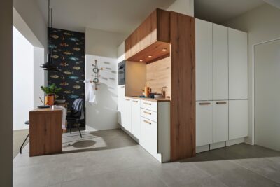 In diesem Apartment wird jeder Winkel genutzt. Die Idee, die Küche um die Ecke zu planen ist dabei neu und sehr hilfreich. Das ist ideal, um tote Ecken oder Nischen optimal zu nutzen. Die Küche aus der Serie „Manhattan“ in „Flair Weiß“ und „Vulkaneiche“ von Nolte Küchen integriert sich perfekt in den Raum.