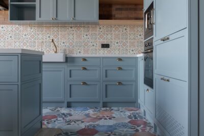 Landhausküche mit farbenfrohen Fliesen – Eine stilvolle Küche im Landhausstil mit blauen Fronten, gemusterten Wandfliesen und einem farbenfrohen Fliesenboden, der dem Raum ein mediterranes Flair verleiht. Foto: Unsplash, Yevhenii Deshko.
